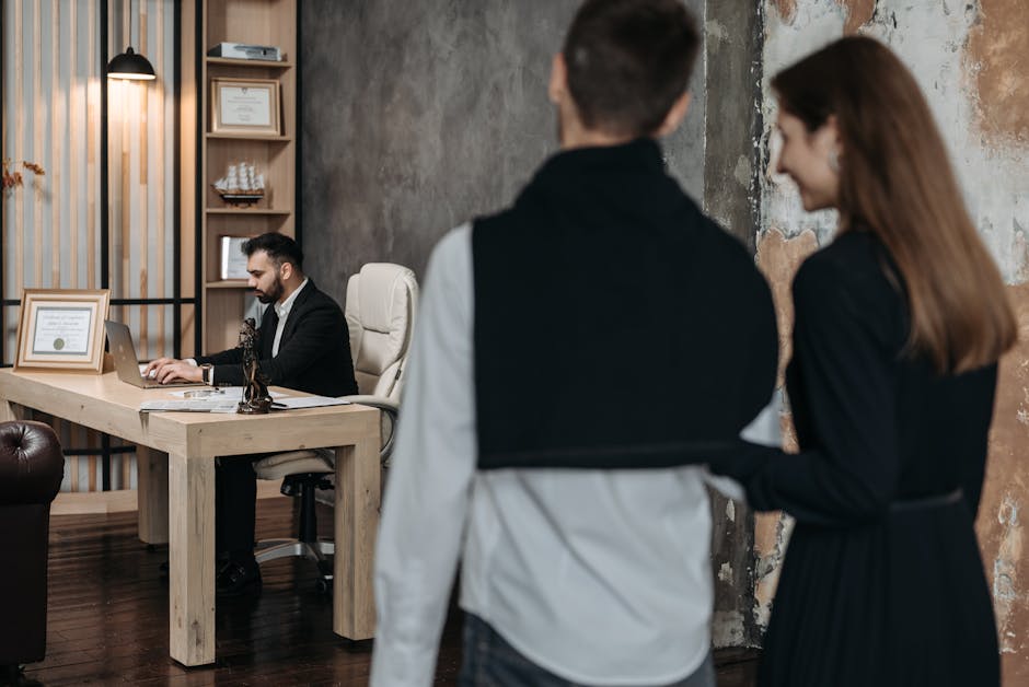 A business consultant working at a desk while a couple in formal wear approaches him in a modern office setting