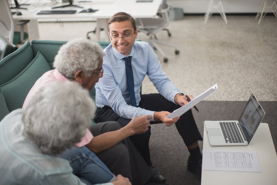 Consultant discussing financial plans with senior clients in a modern office setting, using documents and a laptop